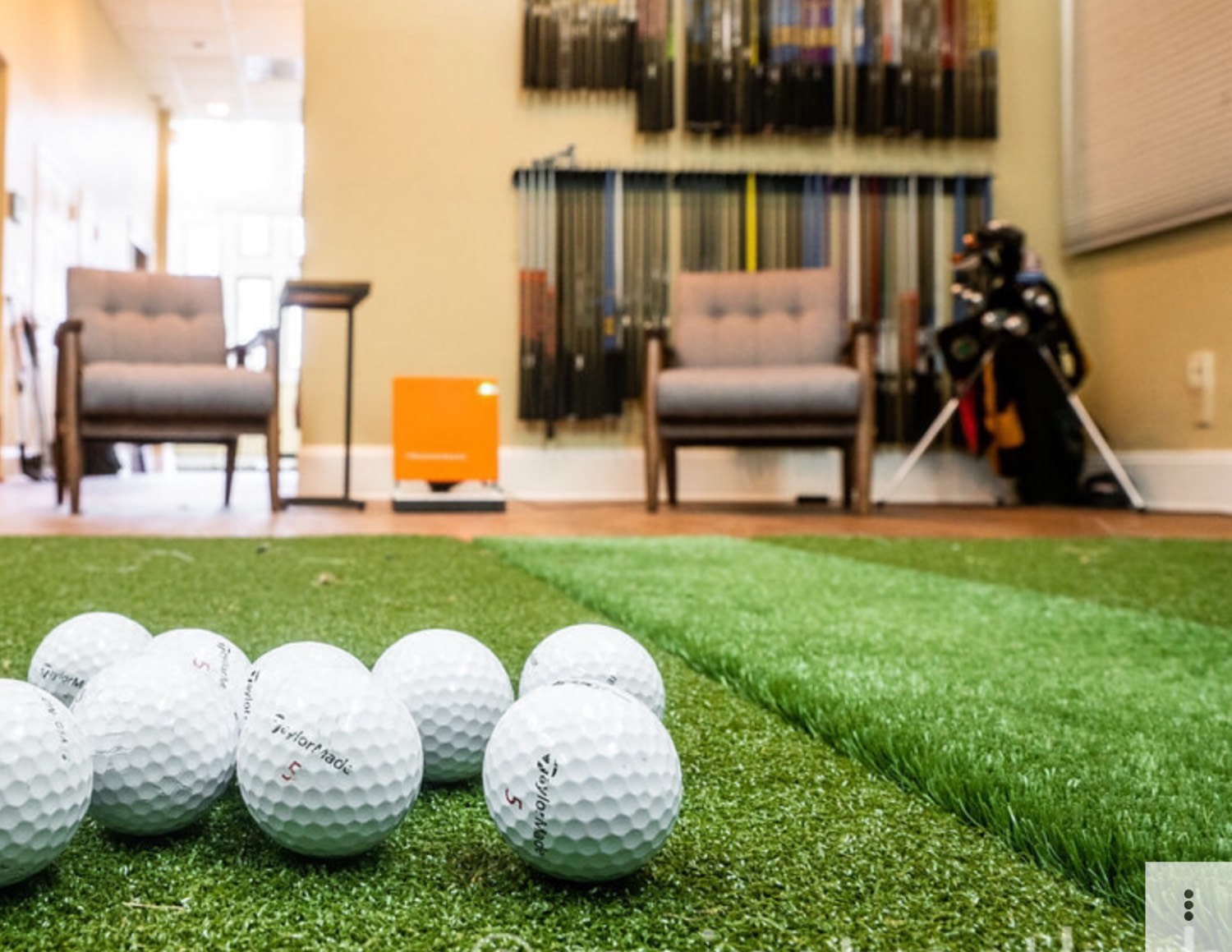 TaylorMade golf balls on the studio turf with the club wall and TrackMan bay behind