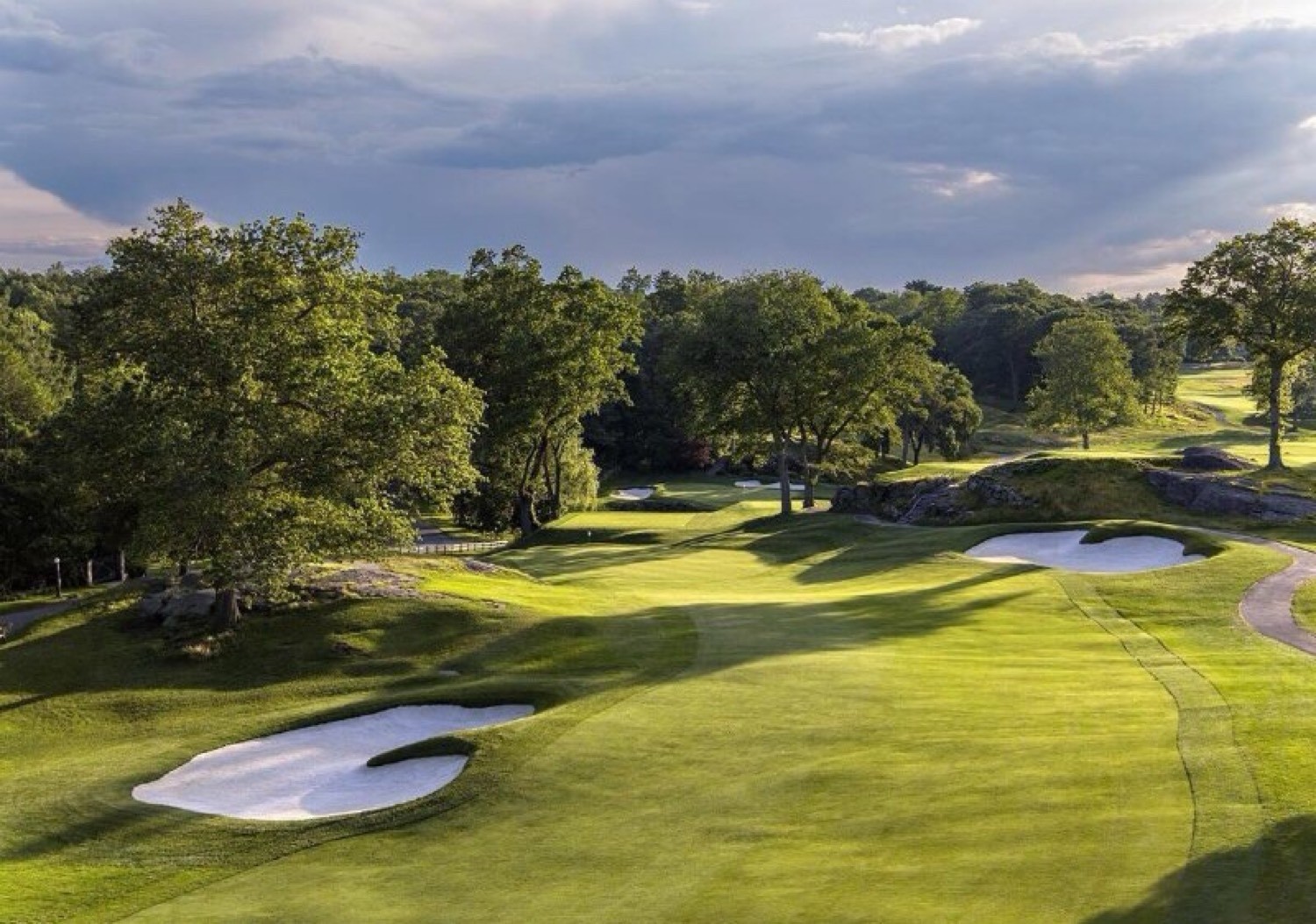 Sunlit golf fairway with sand bunkers under a stormy sky